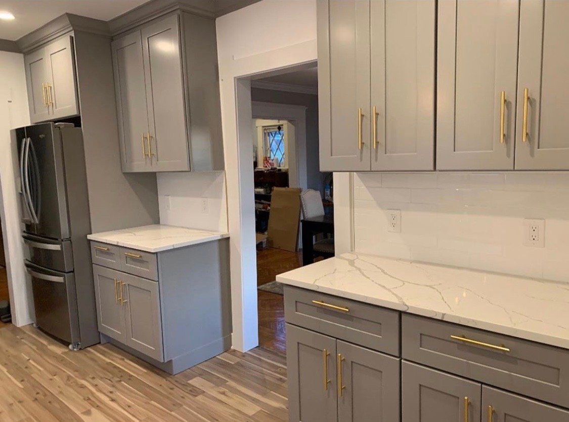 A kitchen with gray cabinets , white counter tops , and a refrigerator.