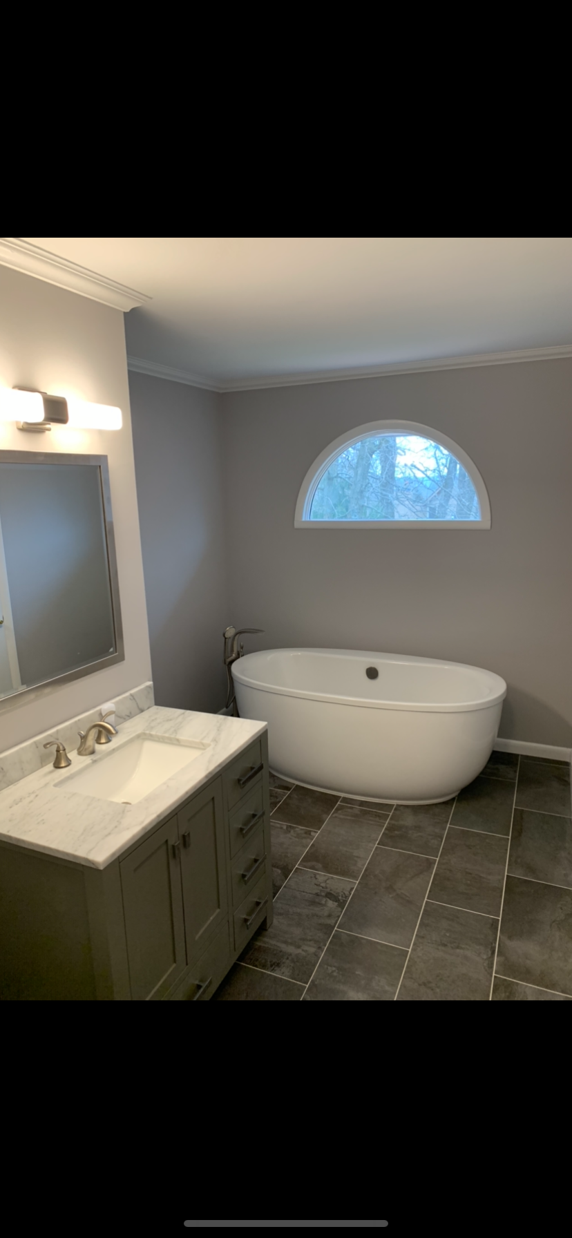 A bathroom with a tub , sink , mirror and window.