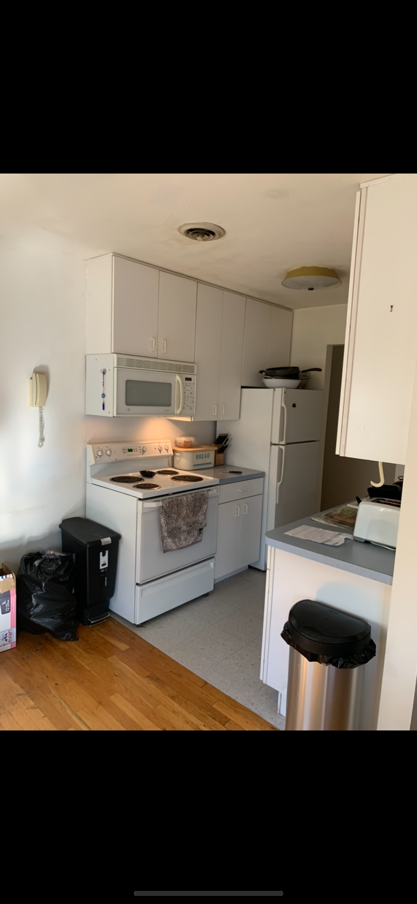 A kitchen with a stove , refrigerator , microwave and trash can.