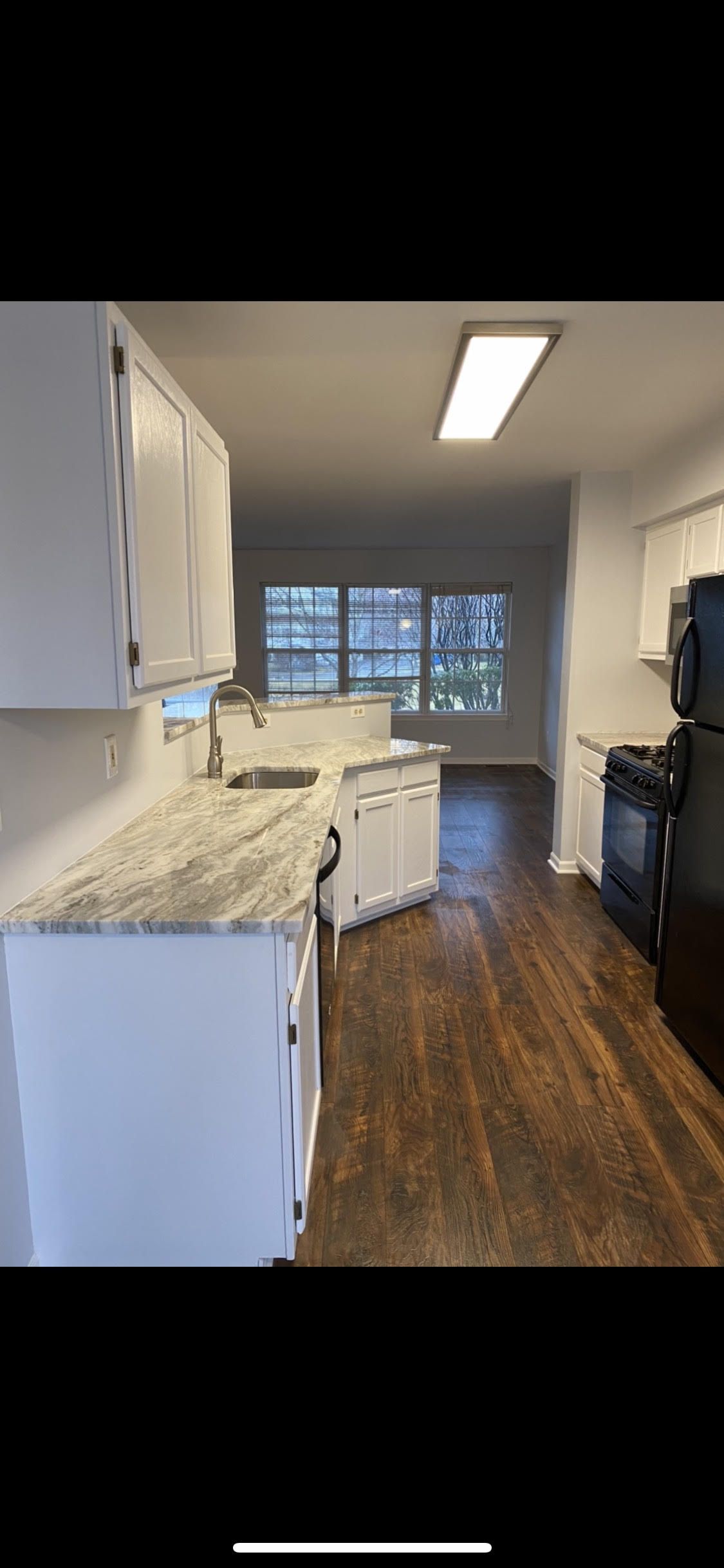 A kitchen with white cabinets , granite counter tops , a black refrigerator and a black stove.
