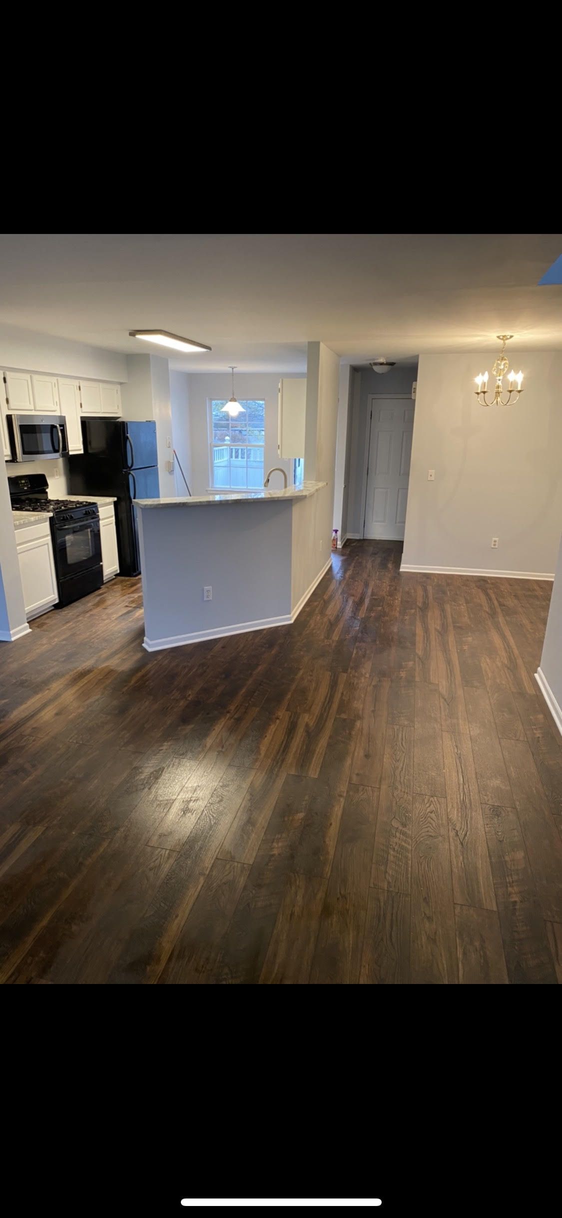 A living room with hardwood floors and a kitchen in the background.