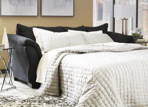 A black couch is turned into a bed in a living room.