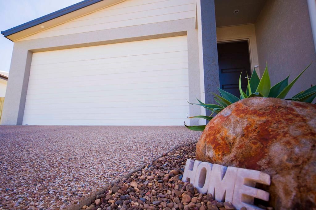 A Sign That Says Home Is On A Rock In Front Of A House And Garage Door — Mick’s Garage Doors In Alice River, QLD