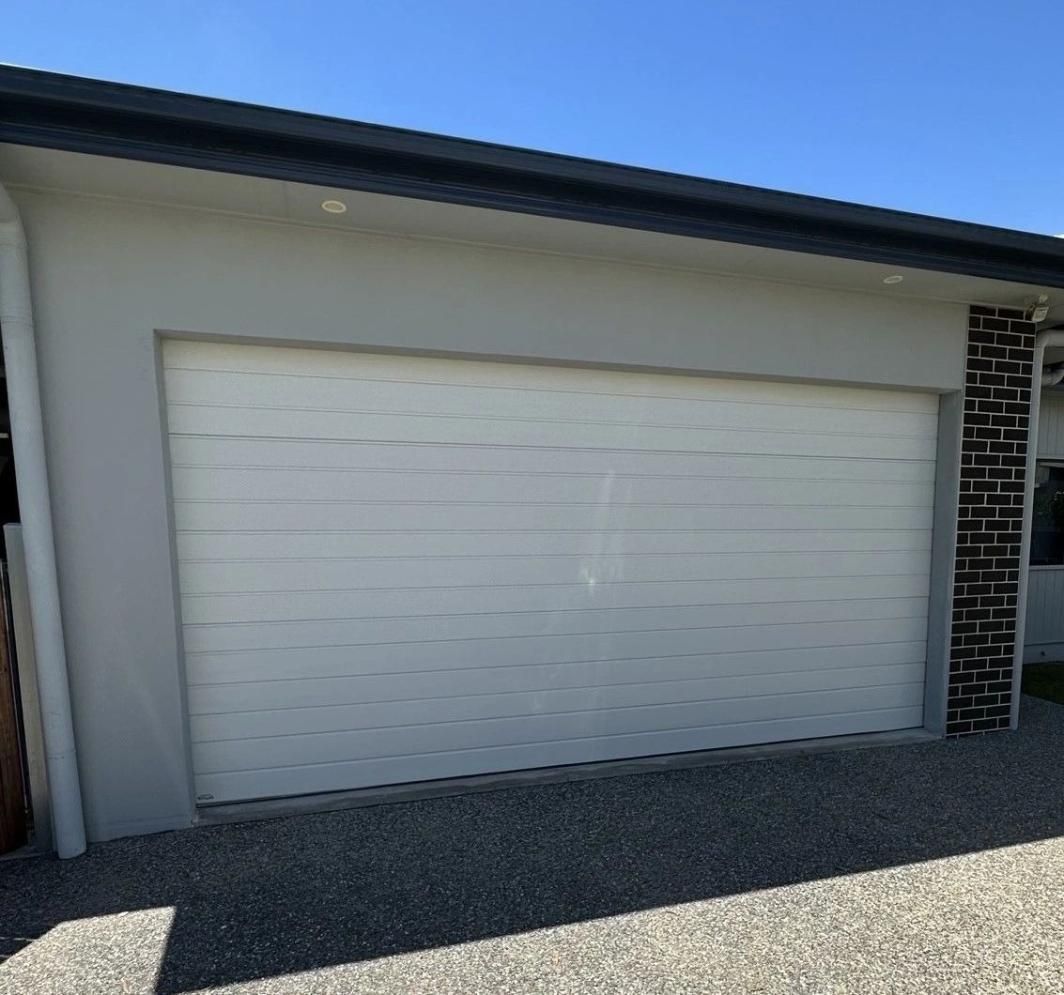 A White Garage Door Is On The Side Of A House — Mick’s Garage Doors In Alice River, QLD