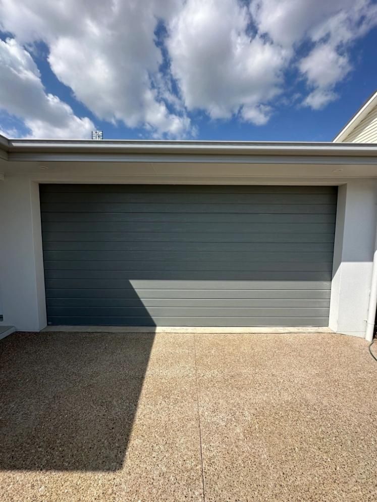 A Gray Garage Door Is Sitting In Front Of A White House — Mick’s Garage Doors In Alice River, QLD