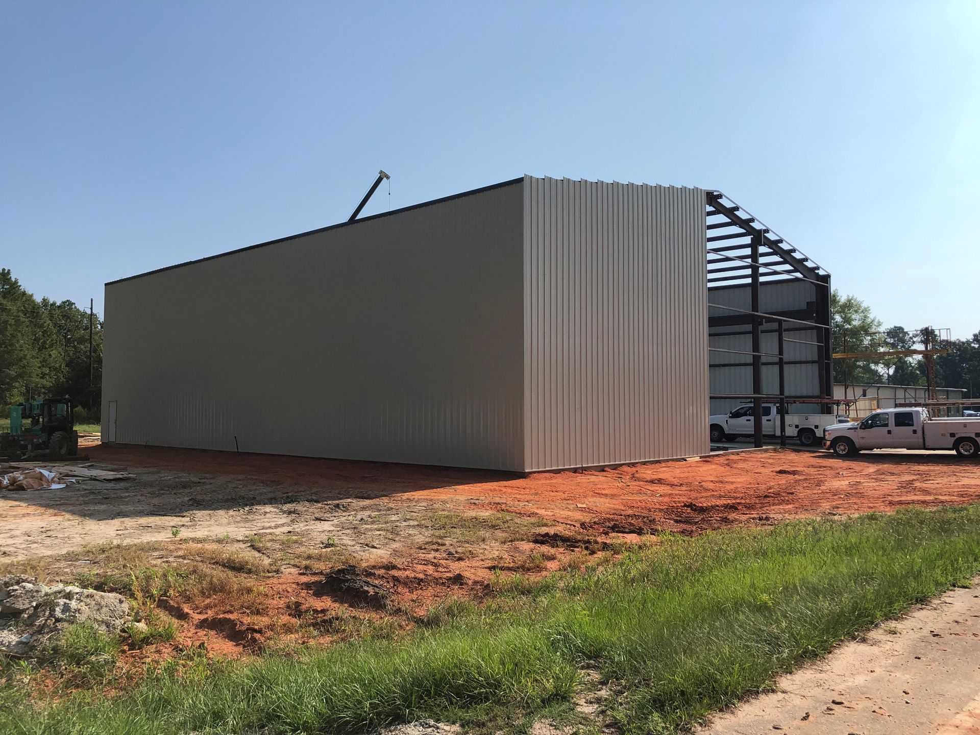 A large metal building is being built next to a dirt road.
