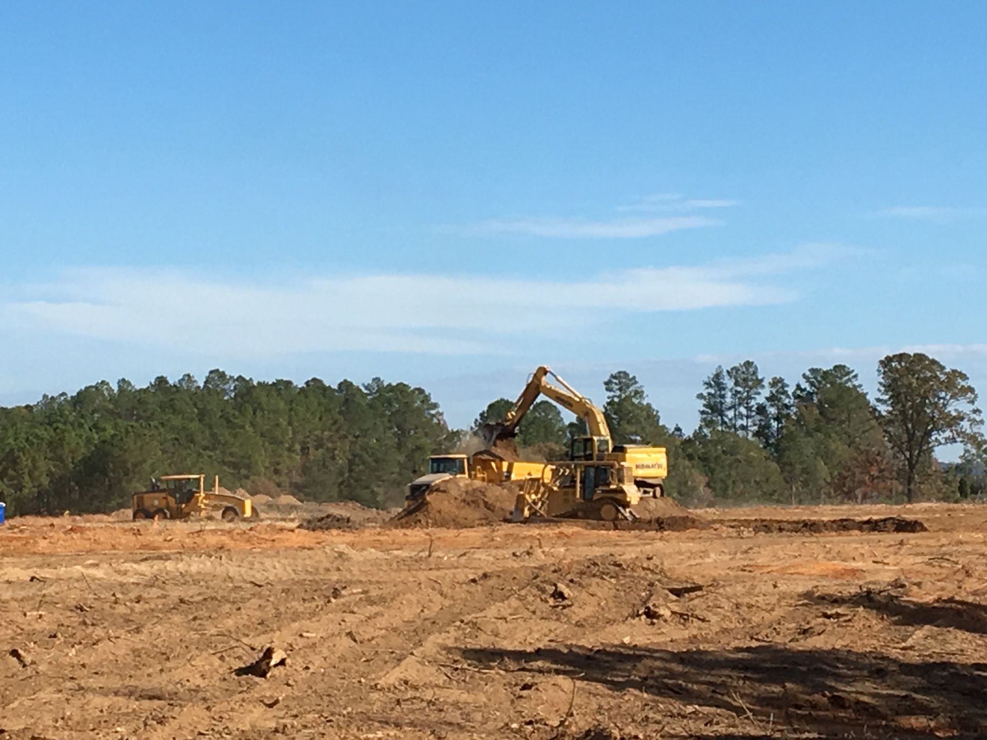 A large yellow excavator is working on a dirt field.