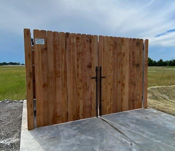 Wooden gate on concrete pad in a grassy field.