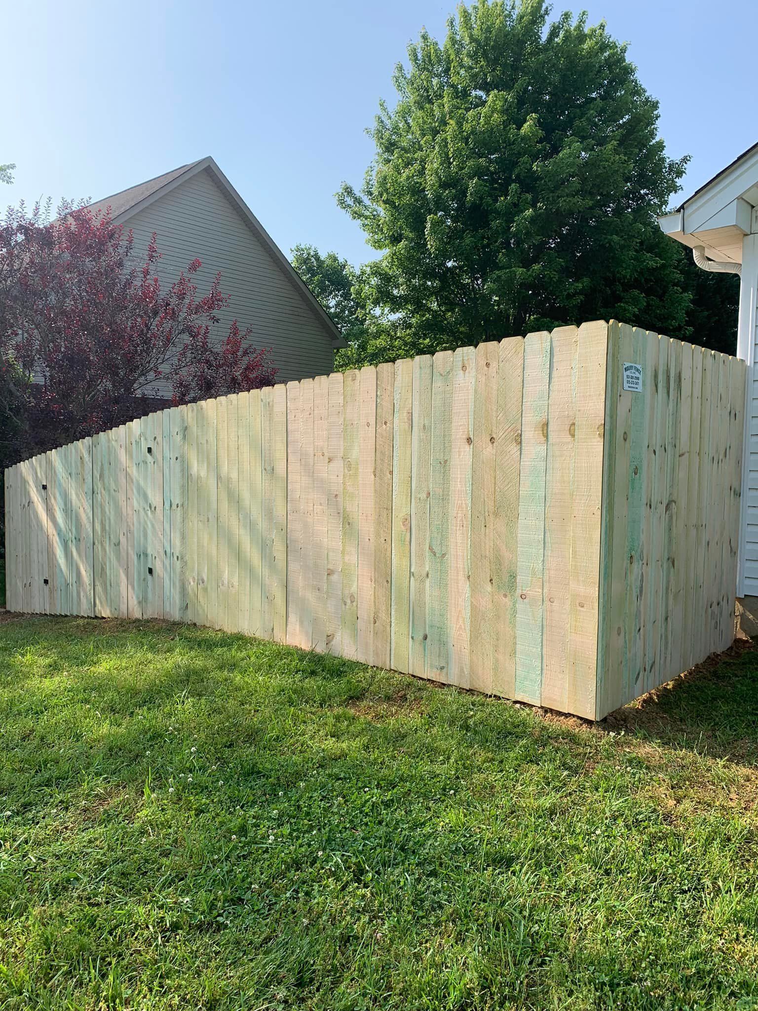 Wooden fence in a grassy yard, with a tree and a house visible in the background.