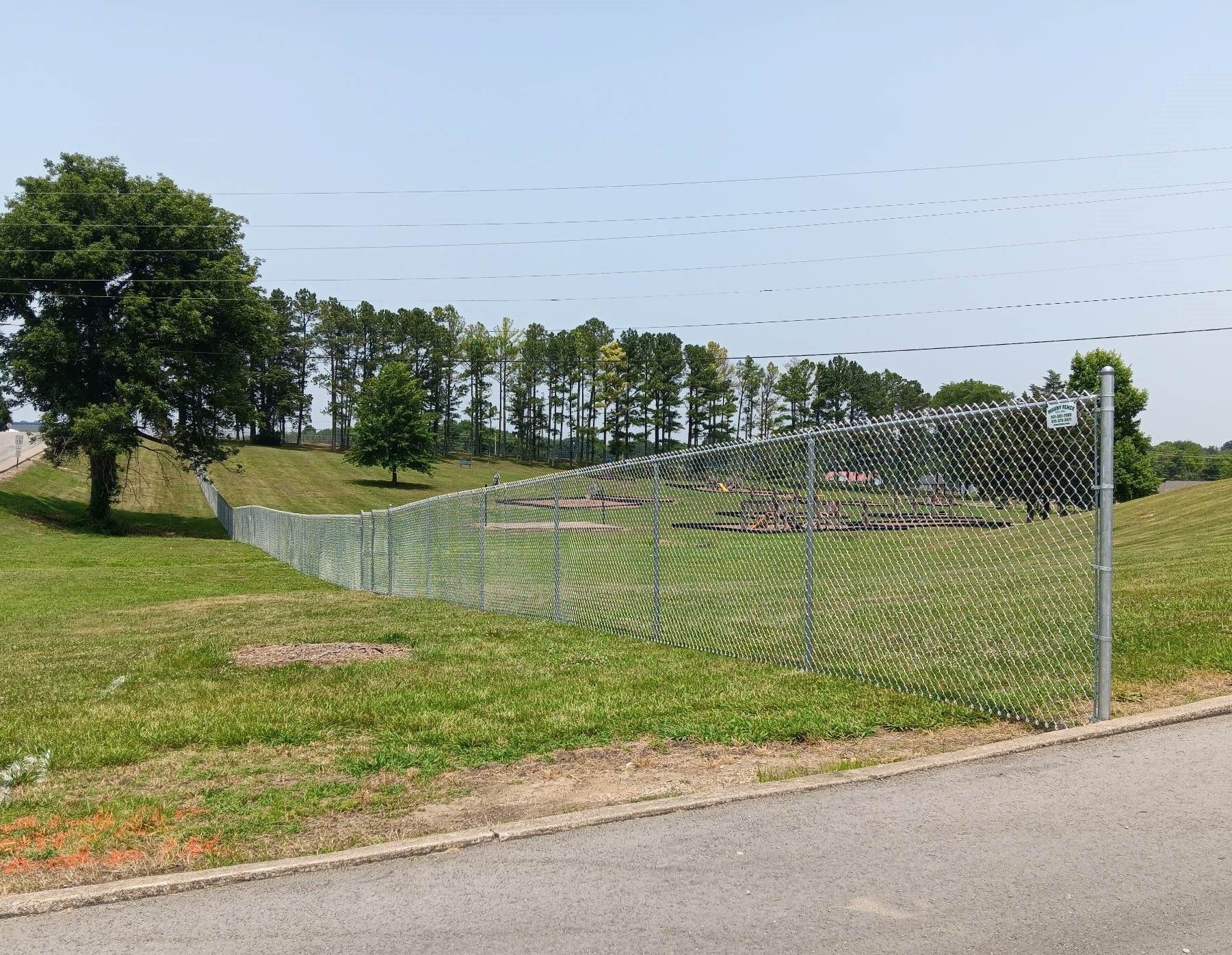 A chain-link fence encloses a grassy area with trees, under a blue sky.