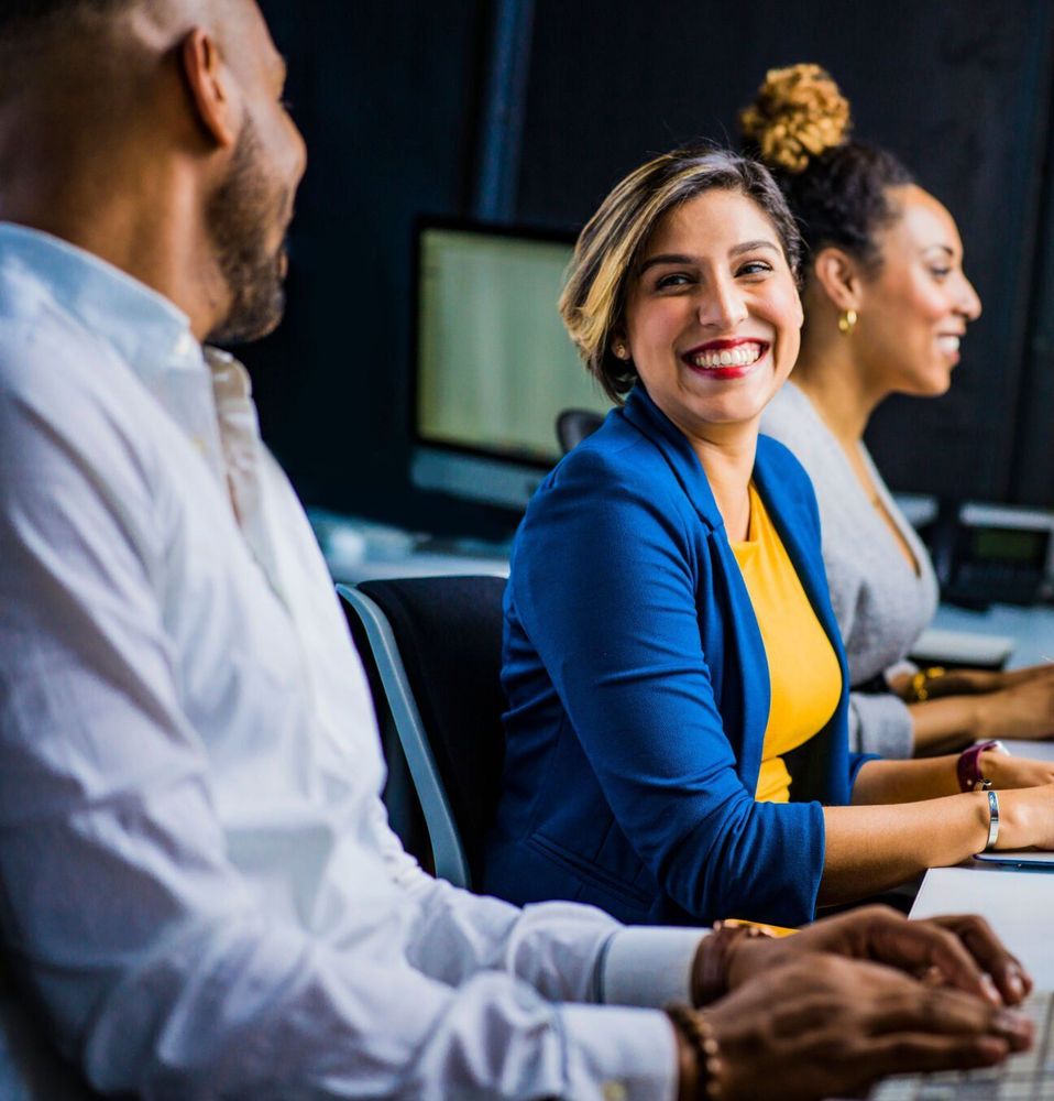 A group of people are sitting in front of computers and smiling.