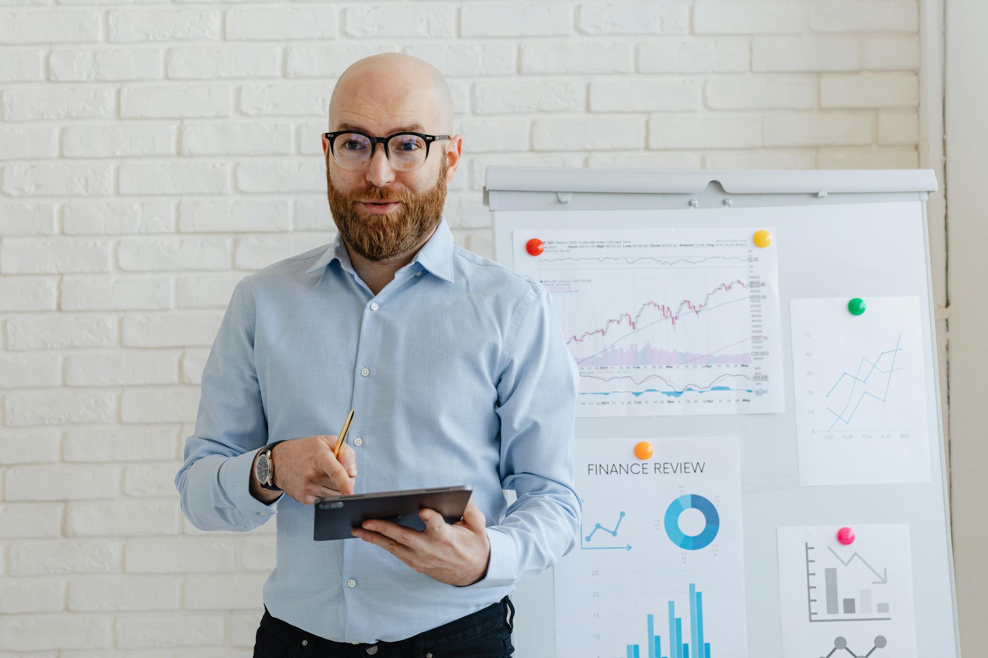 A man with a beard is holding a tablet in front of a whiteboard.