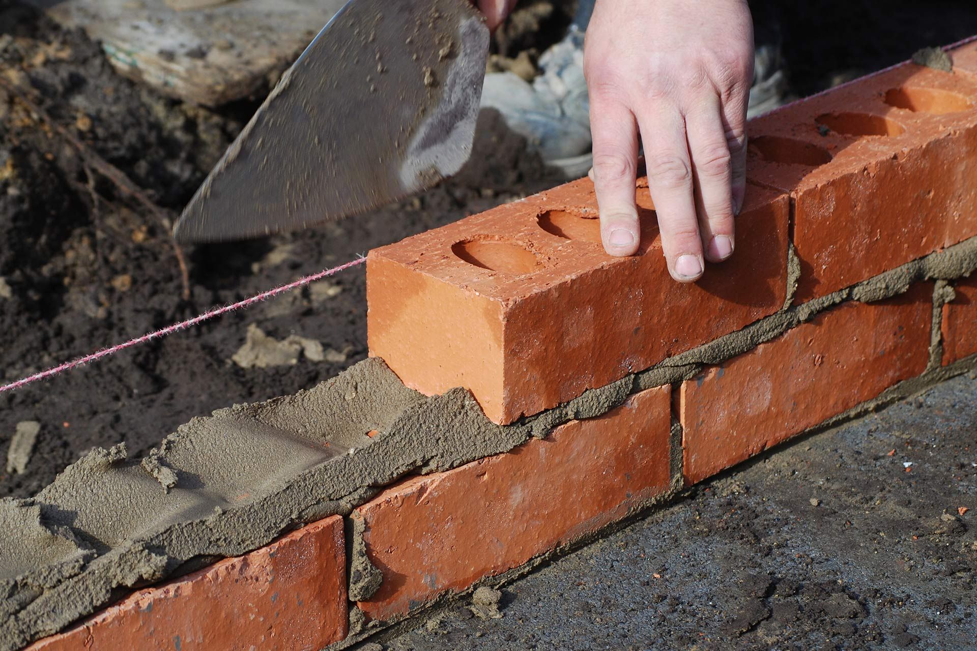 A bricklayer lays a brick, using a trowel to spread mortar onto the existing bricks.