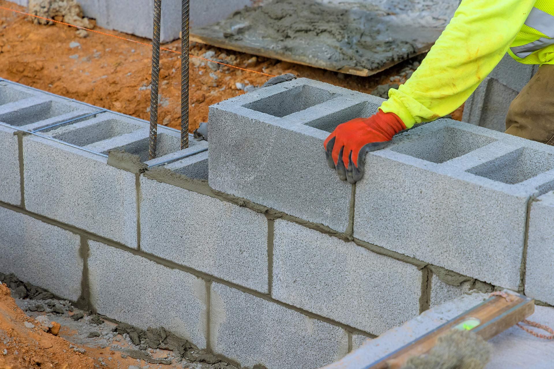 Person in yellow and red gloves laying concrete blocks for a wall at a construction site.