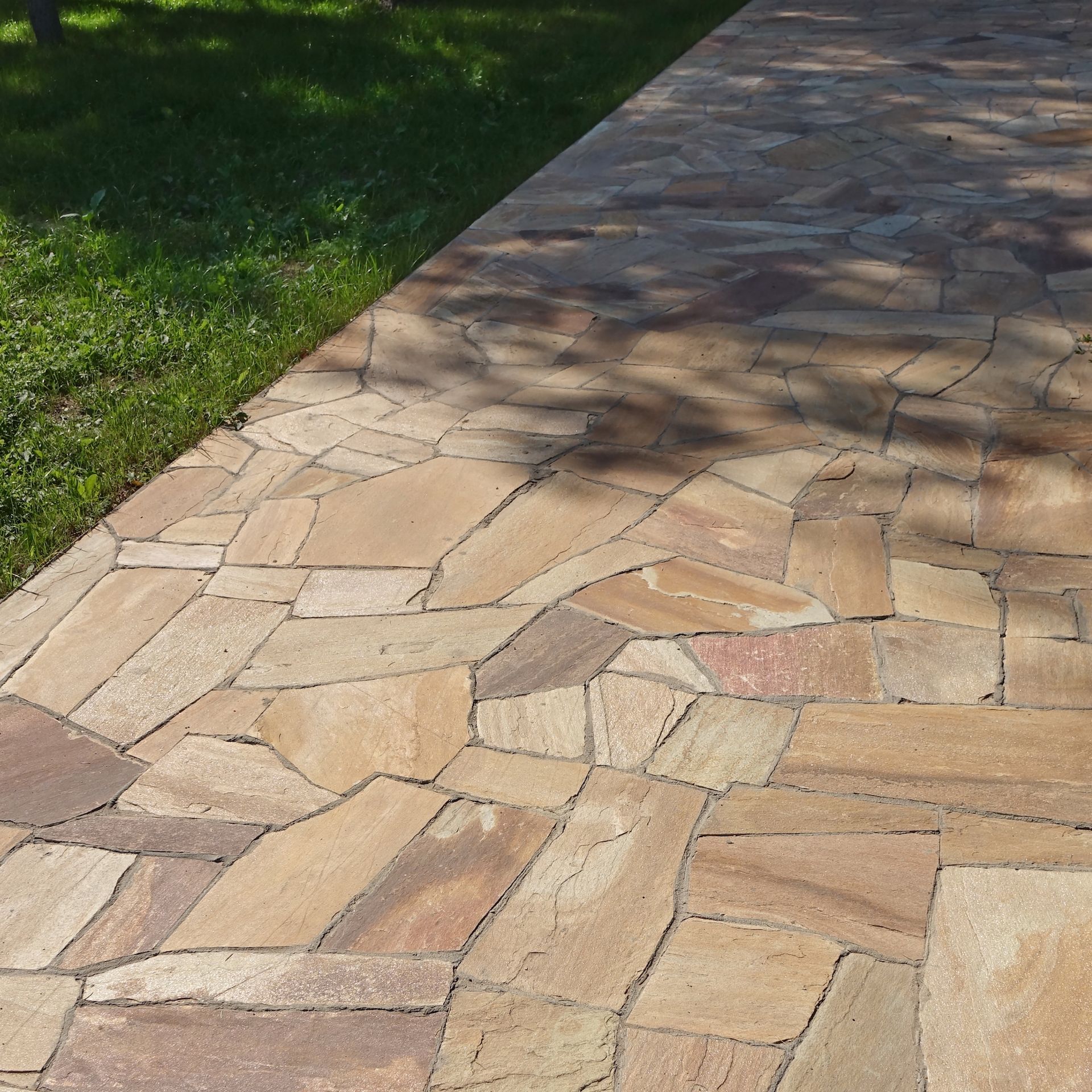 Flagstone path next to grass; tan, brown, and gray irregular stones.