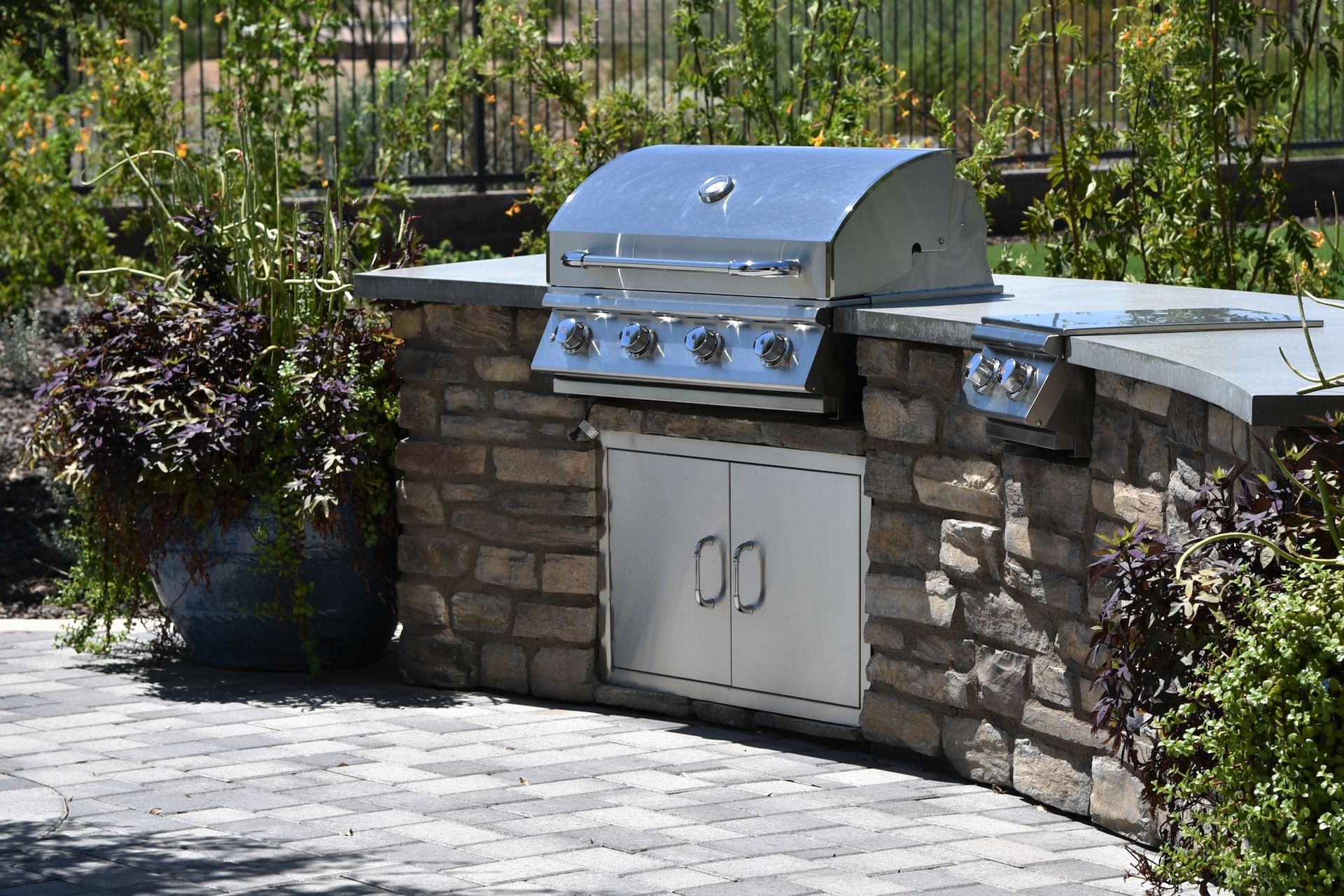 Outdoor stone grilling station with a stainless steel grill and storage doors.