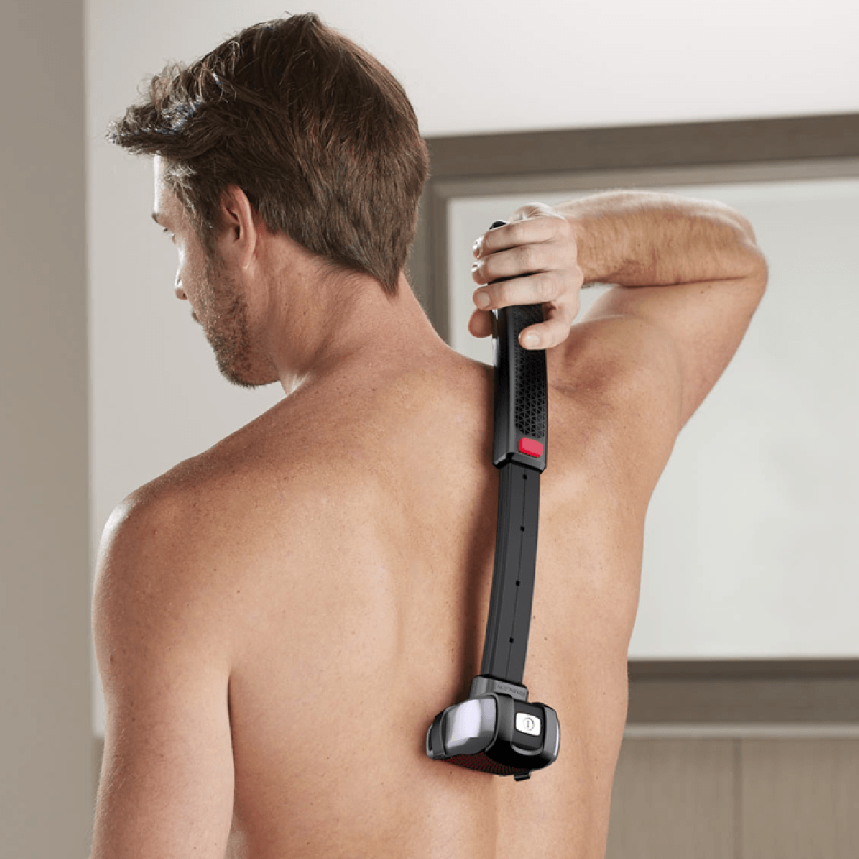 Man shaving his back with a long-handled razor in a bathroom.