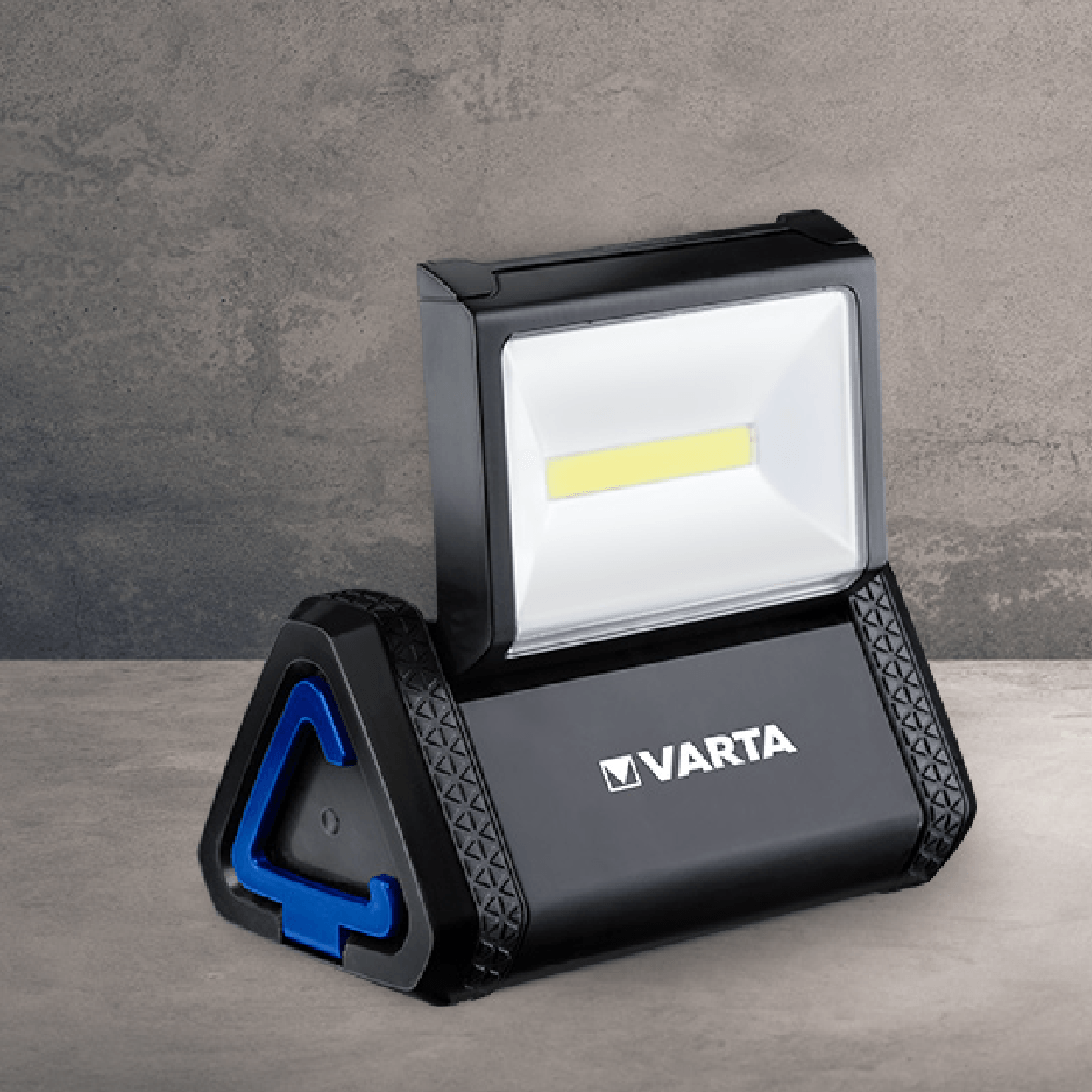Black and blue VARTA LED work light on a concrete surface, angled, showing the light and handle.