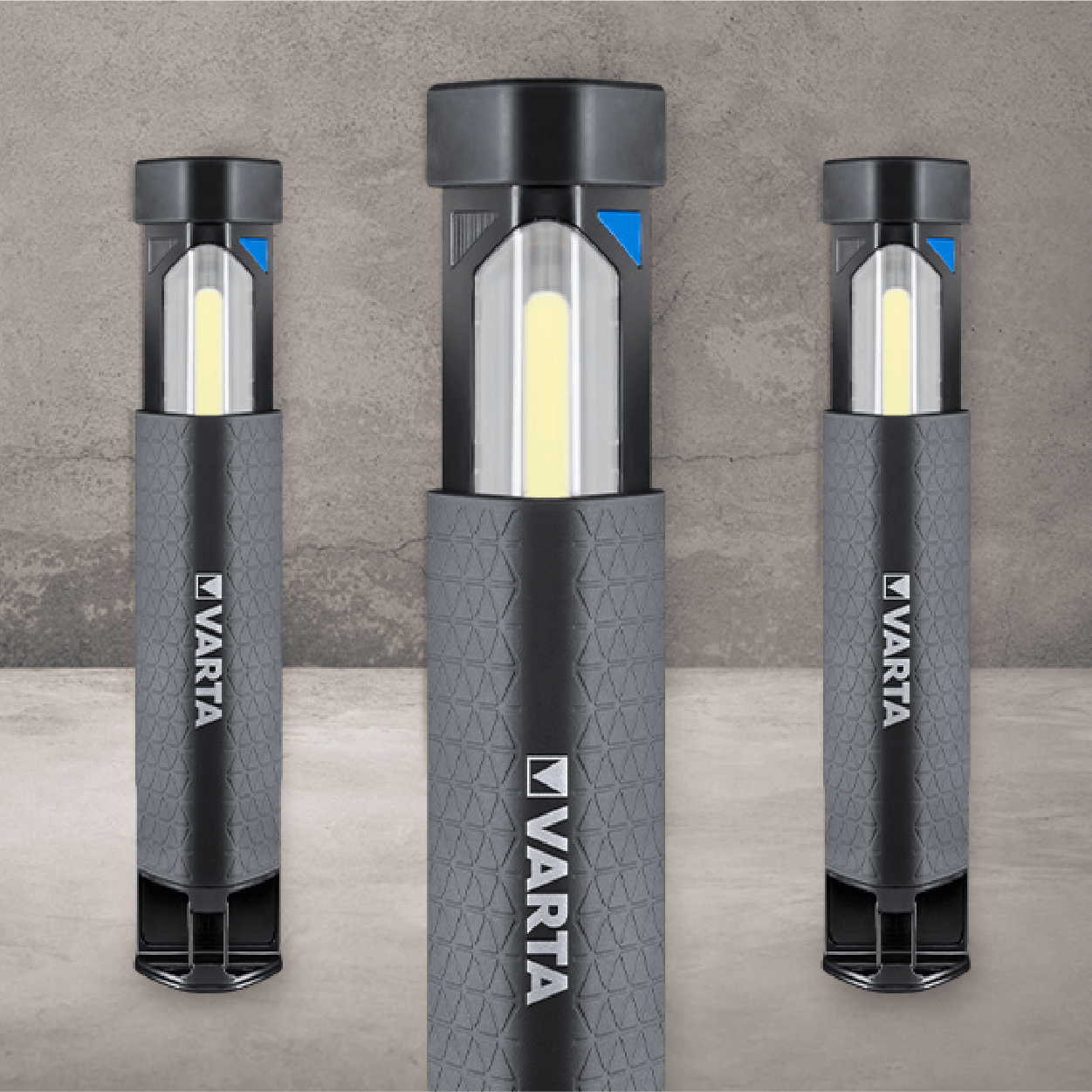 Three Varta work lights, cylindrical with dark gray bodies, centered on a gray wall.