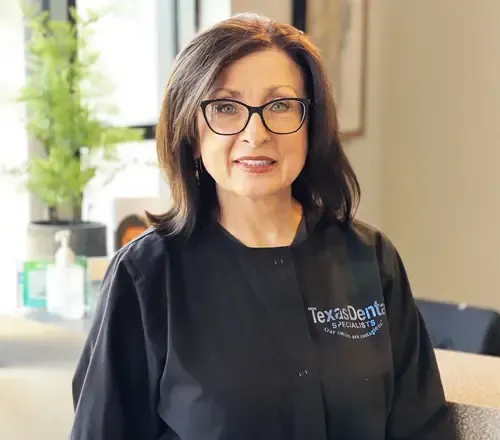 olga wearing glasses and a black coat is standing in a room.