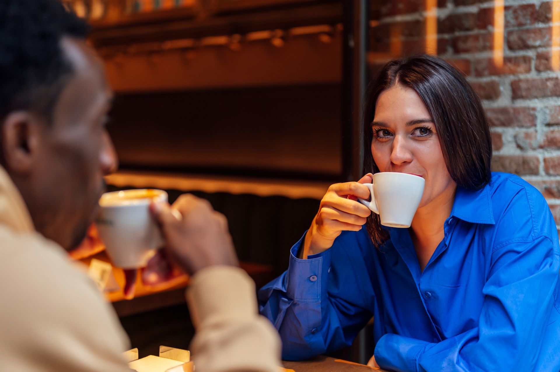 A man and a woman are sitting at a table drinking coffee.