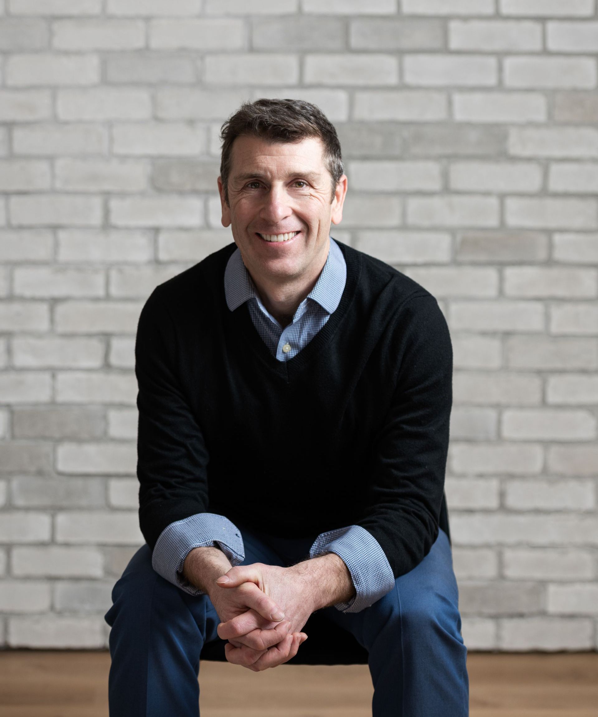 a man is sitting on the floor with his hands folded in front of a brick wall .