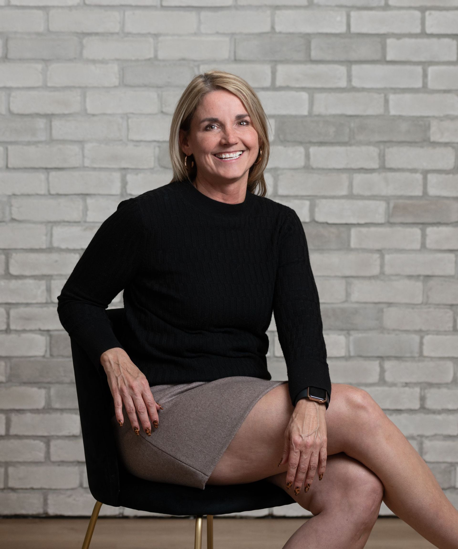 a woman is sitting in a chair with her legs crossed in front of a brick wall .