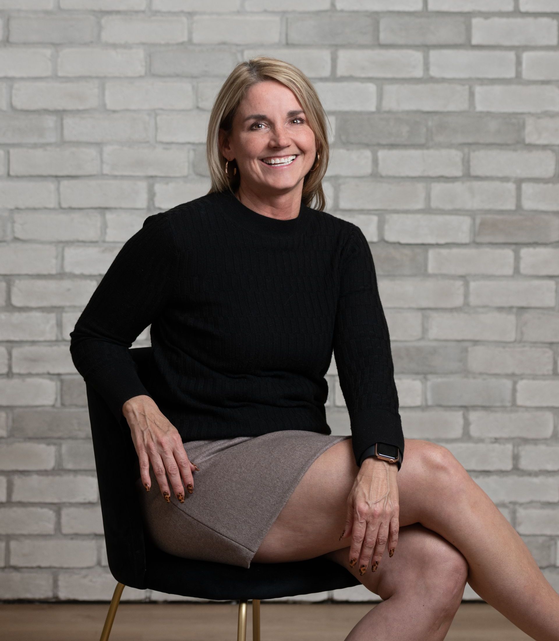 a woman is sitting in a chair with her legs crossed in front of a brick wall .