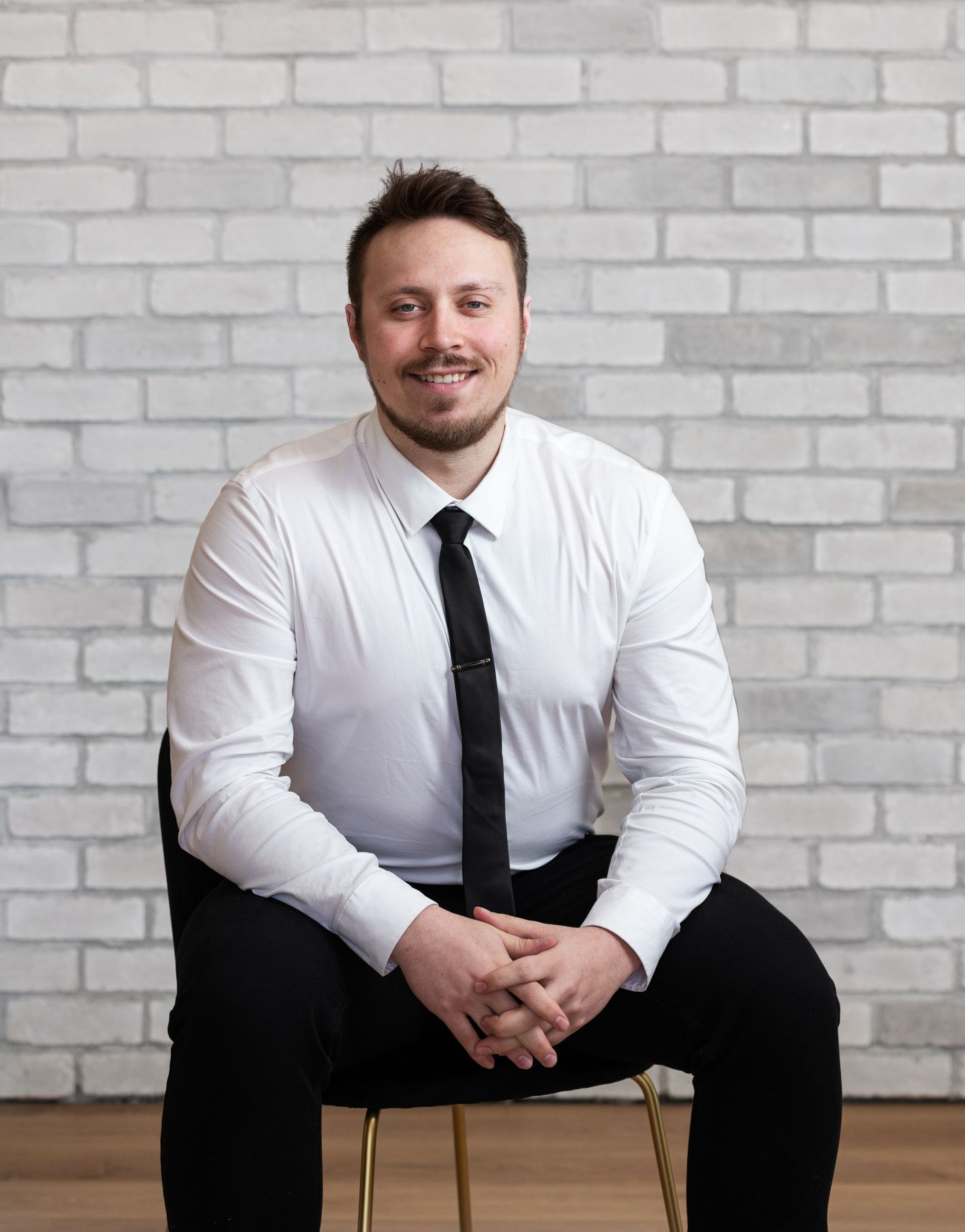 a man in a white shirt and black tie is sitting on a chair in front of a brick wall .
