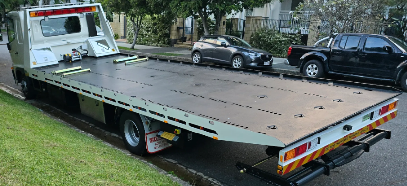 A tow truck with a flat bed is parked on the side of the road.