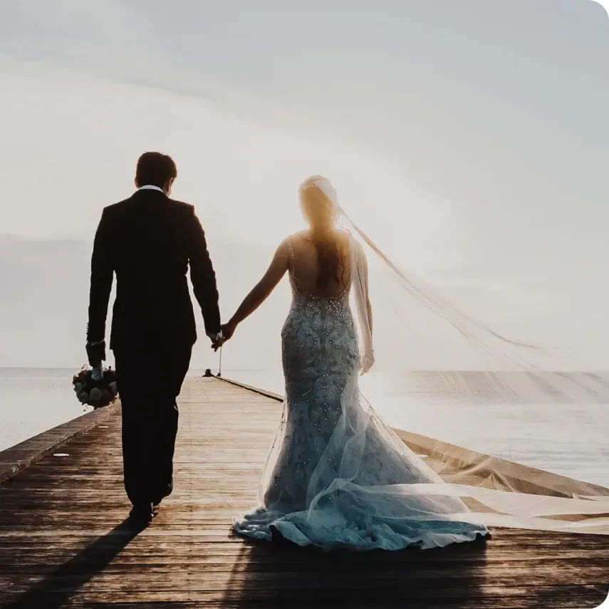 A bride and groom walking on a pier holding hands