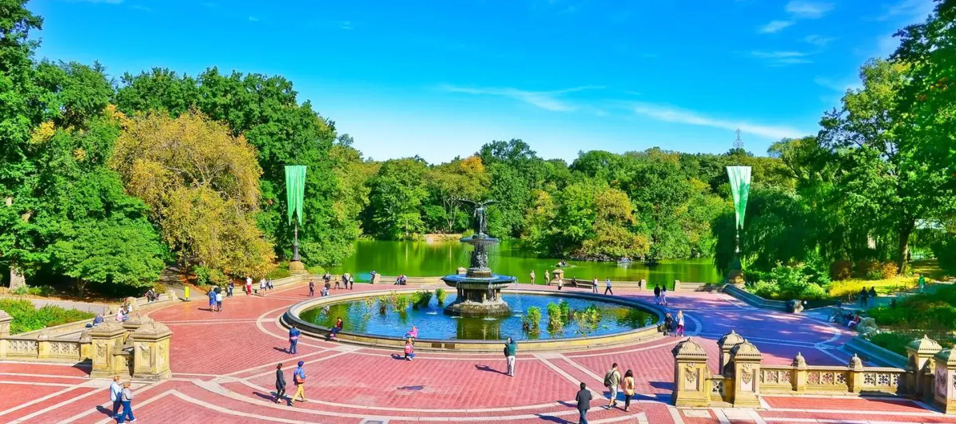 A group of people are walking around a fountain in a park.