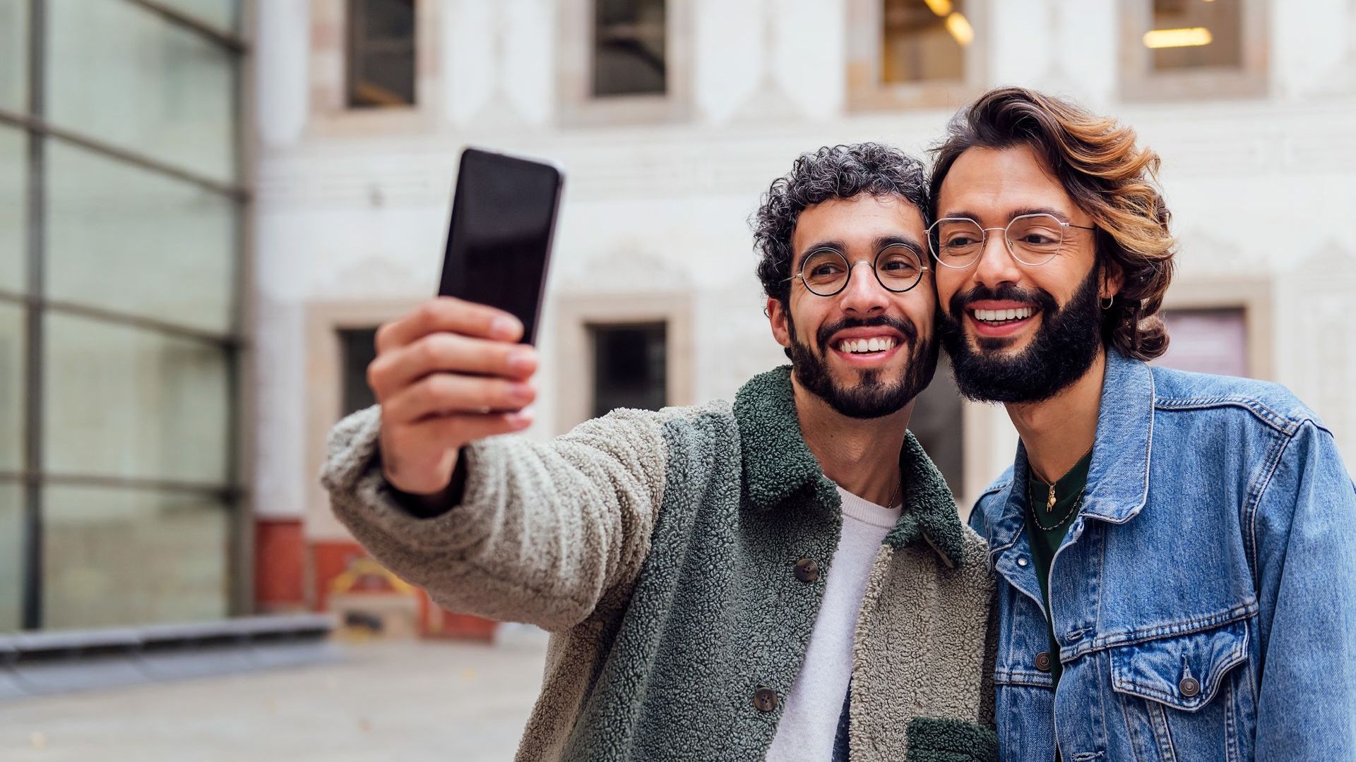 Two men are taking a selfie with a cell phone.