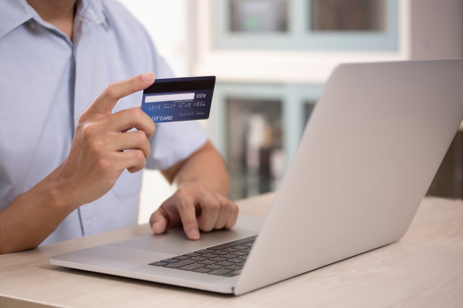 A man is holding a credit card while using a laptop computer.