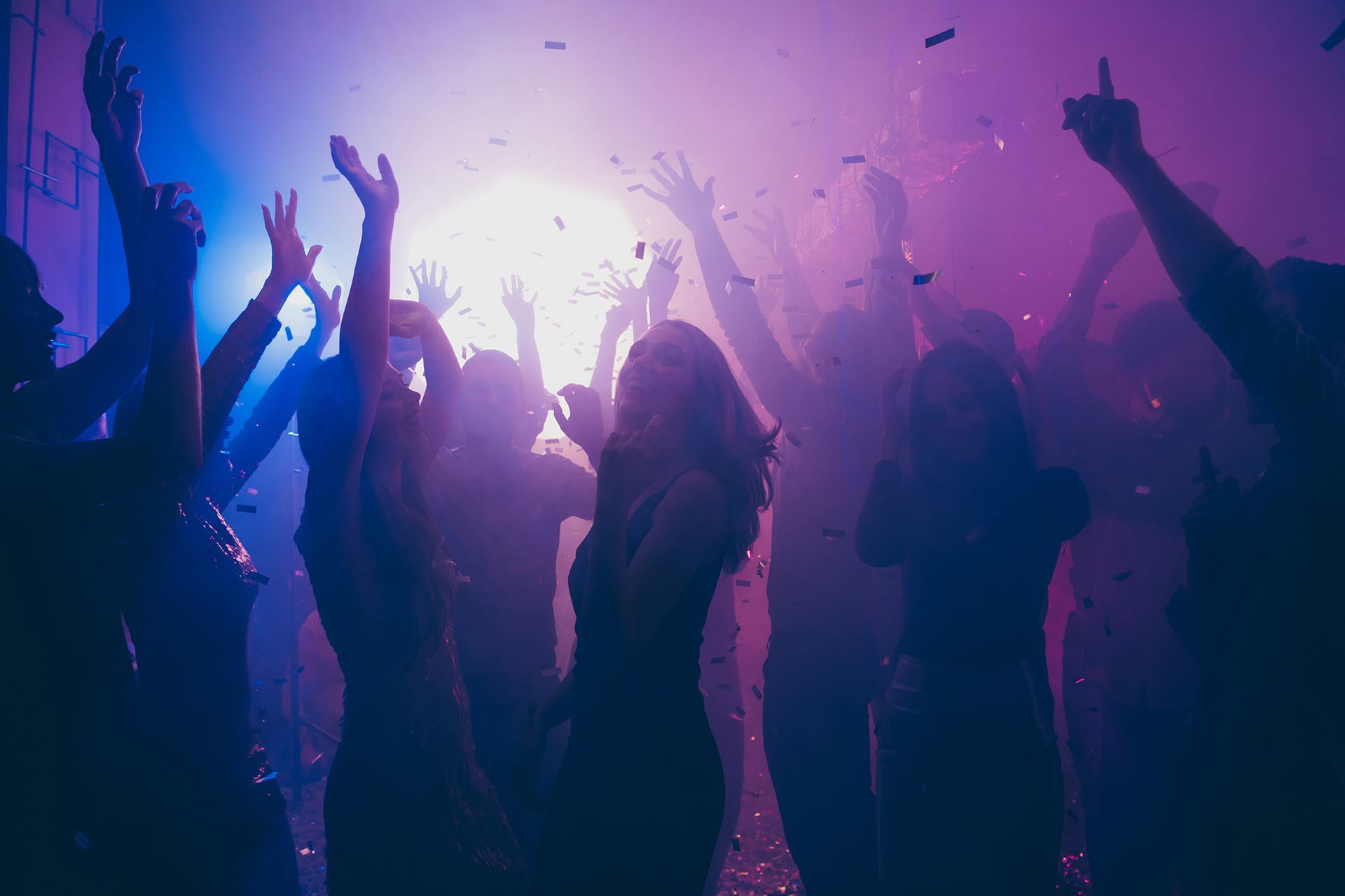 A group of people are dancing in a club with their hands in the air.