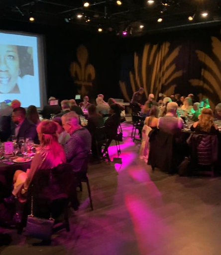 A large group of people are sitting at tables in a dark room