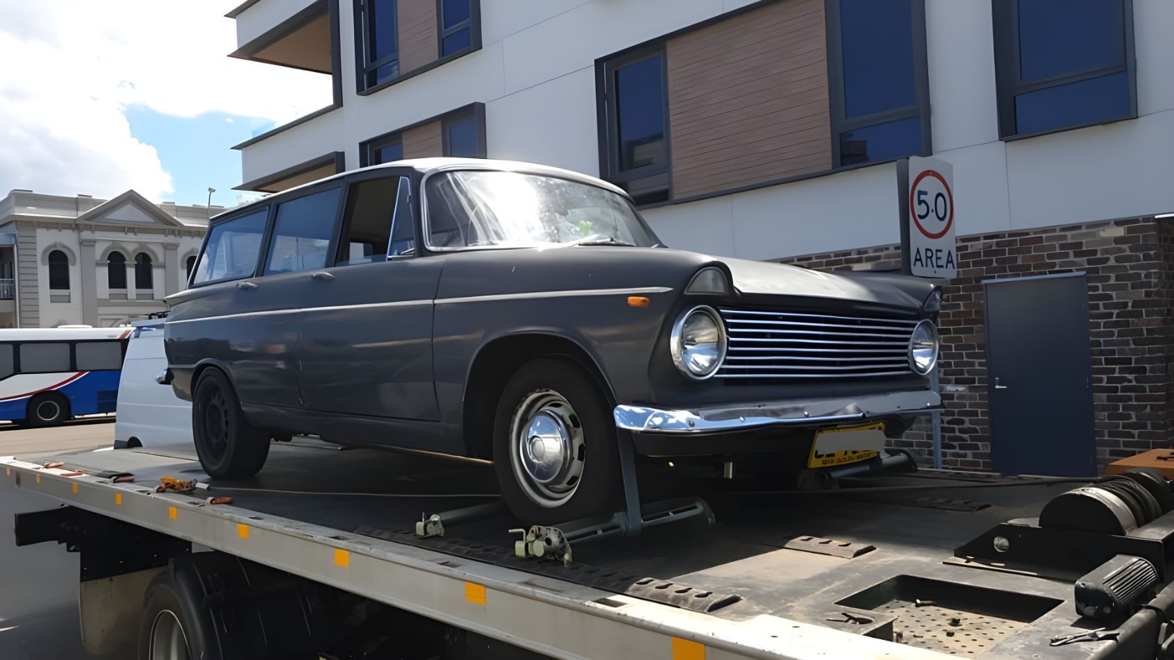 An Old Car Is Sitting On Top Of A Tow Truck — NCM Towing Newcastle In Lake Macquarie, NSW