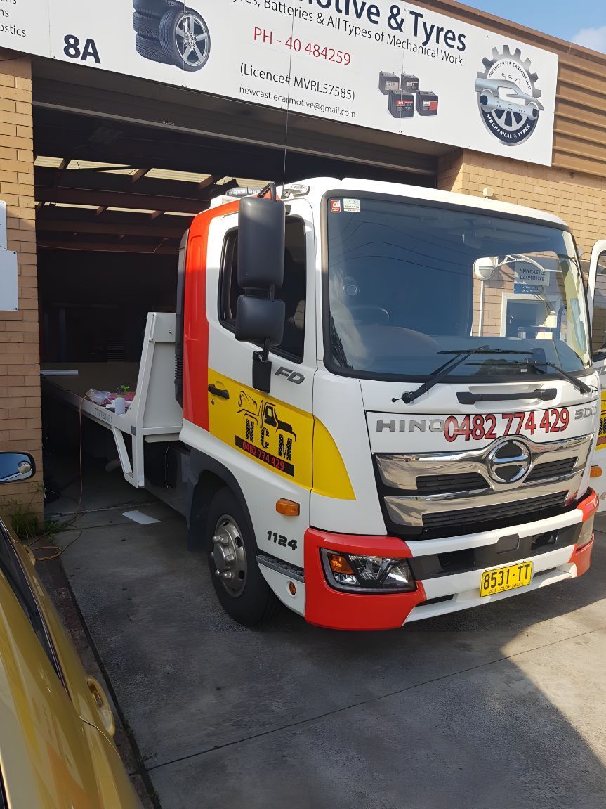 A White And Red Tow Truck Is Parked In Front Of A Garage — NCM Towing Newcastle In Broadmeadow, NSW