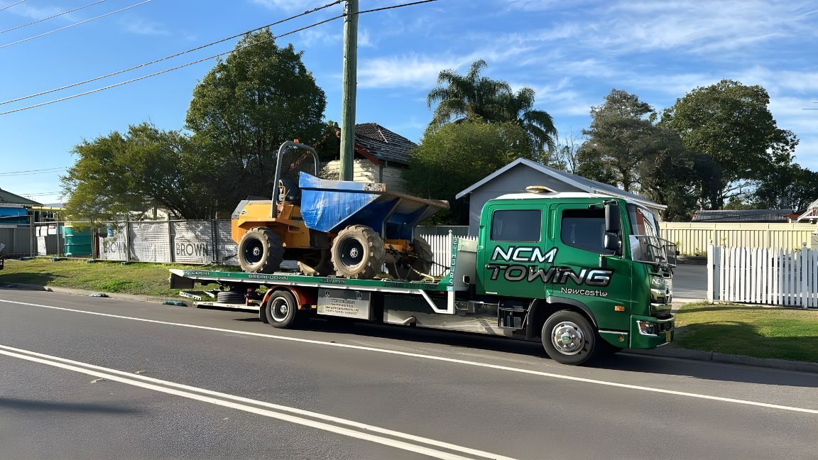 A Tow Truck With A Dump Truck On The Back Is Parked On The Side Of The Road — NCM Towing Newcastle In Stockton, NSW