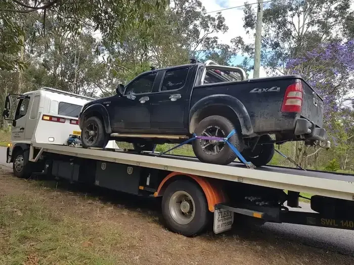 A Black Truck Is Being Towed By A Tow Truck — NCM Towing Newcastle In Central Coast, NSW
