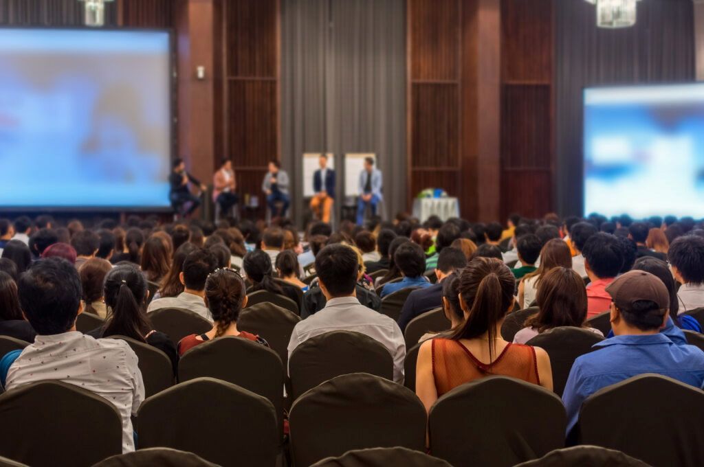 Audience Seated in a Large Conference Room, Watching Speakers on a Stage With Screens — Coastal Vibez In Sydney, NSW