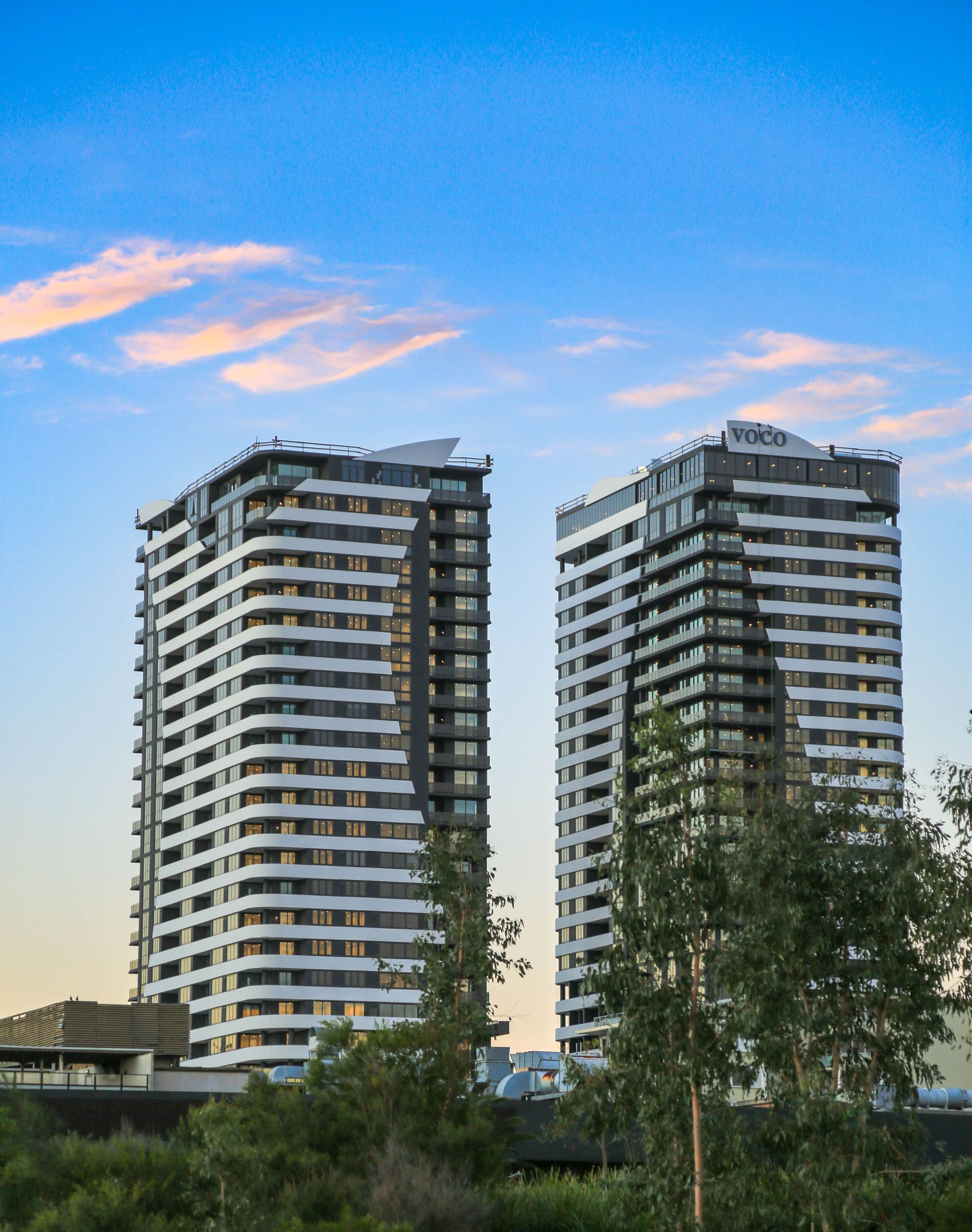 Two large black and white apartment buildings with trees in front of them and clouds above them — Coastal Vibez In The Entrance, NSW