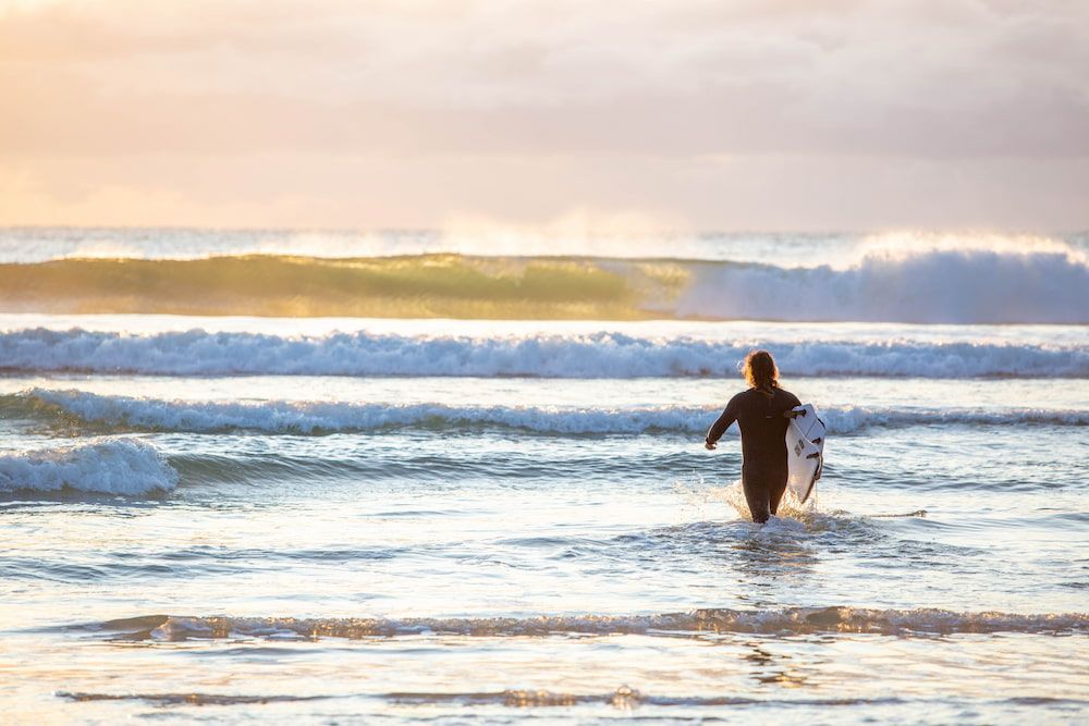 A Surfer is Walking Out of the Ocean With His Surfboard — Coastal Vibez In The Entrance, NSW