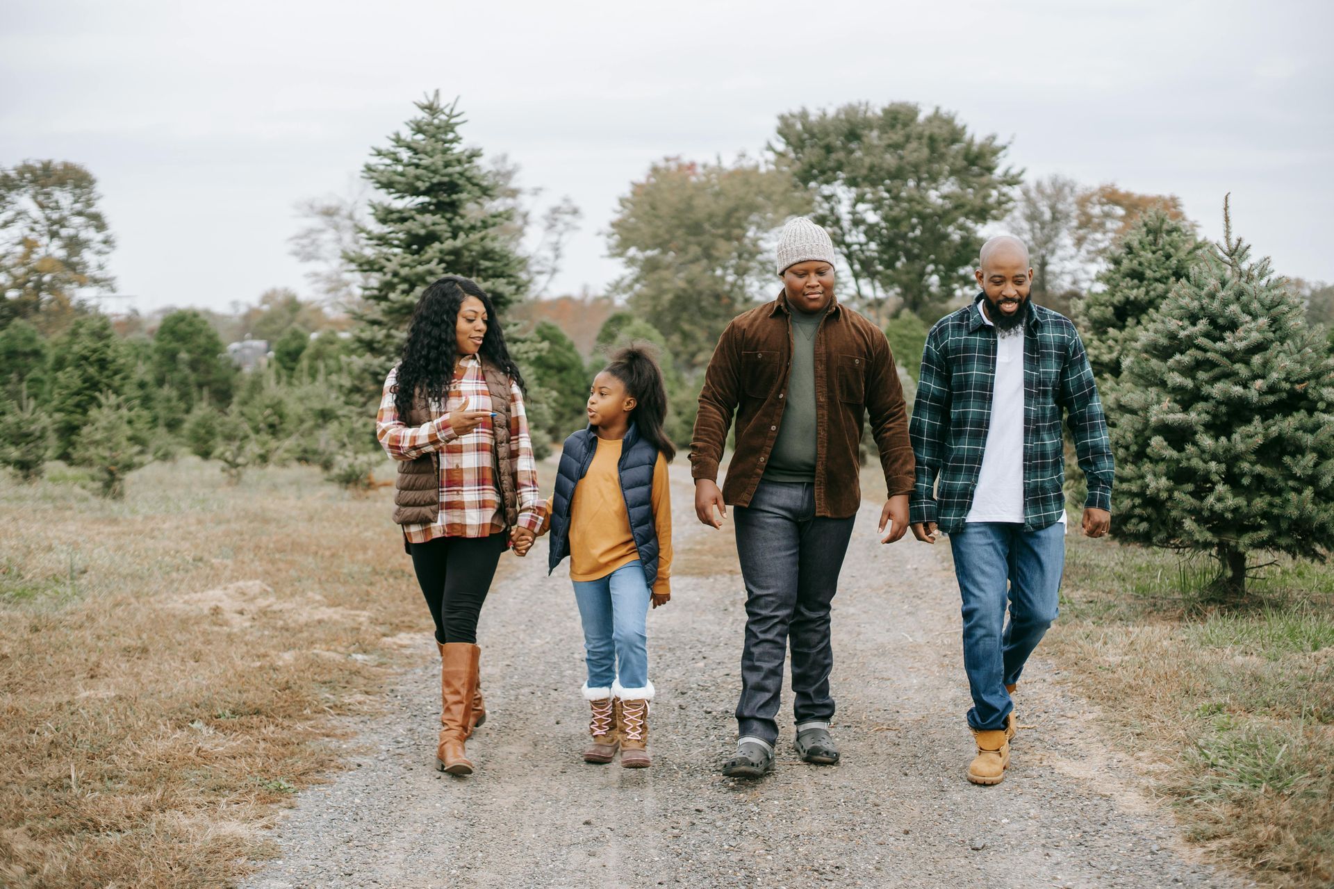 Family walking down a path in a field of Christmas trees. They are wearing coats and boots.