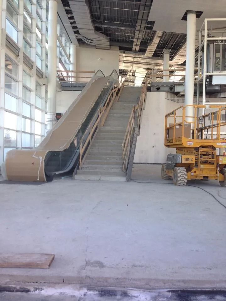 Cantiere edile al coperto con due scale mobili in fase di installazione e un ascensore giallo accanto ad esse.