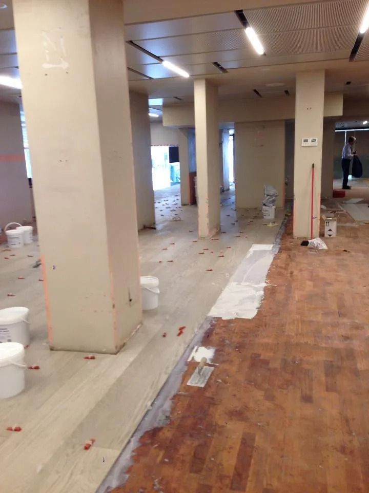Corridoio interno con pavimento danneggiato, detriti e area di cantiere a vista accanto a colonne color crema.
