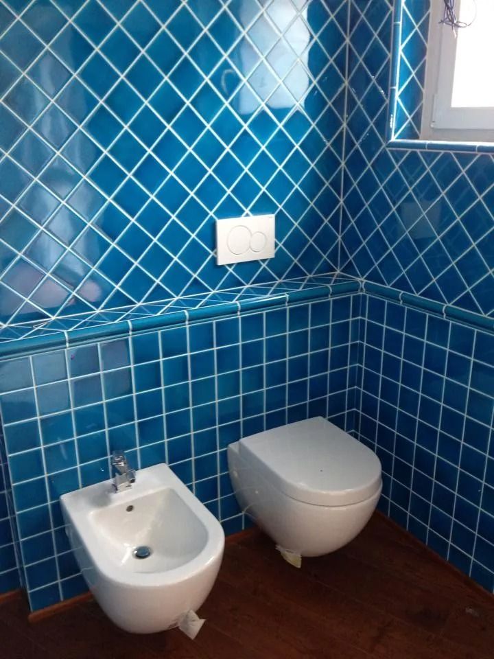 Bagno piastrellato di blu con bidet, WC sospeso e pavimento in legno.