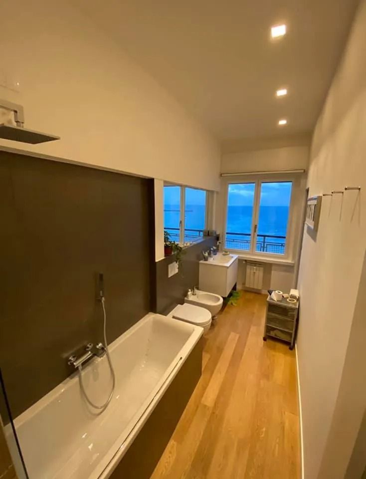 Bagno moderno con vasca freestanding, doccia, pavimento in legno e ampie finestre con vista sull'acqua.