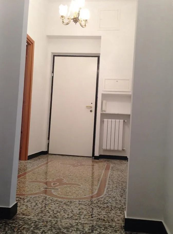 Corridoio con porta bianca, pavimento in piastrelle decorate, lampadario e nicchia per il termosifone.