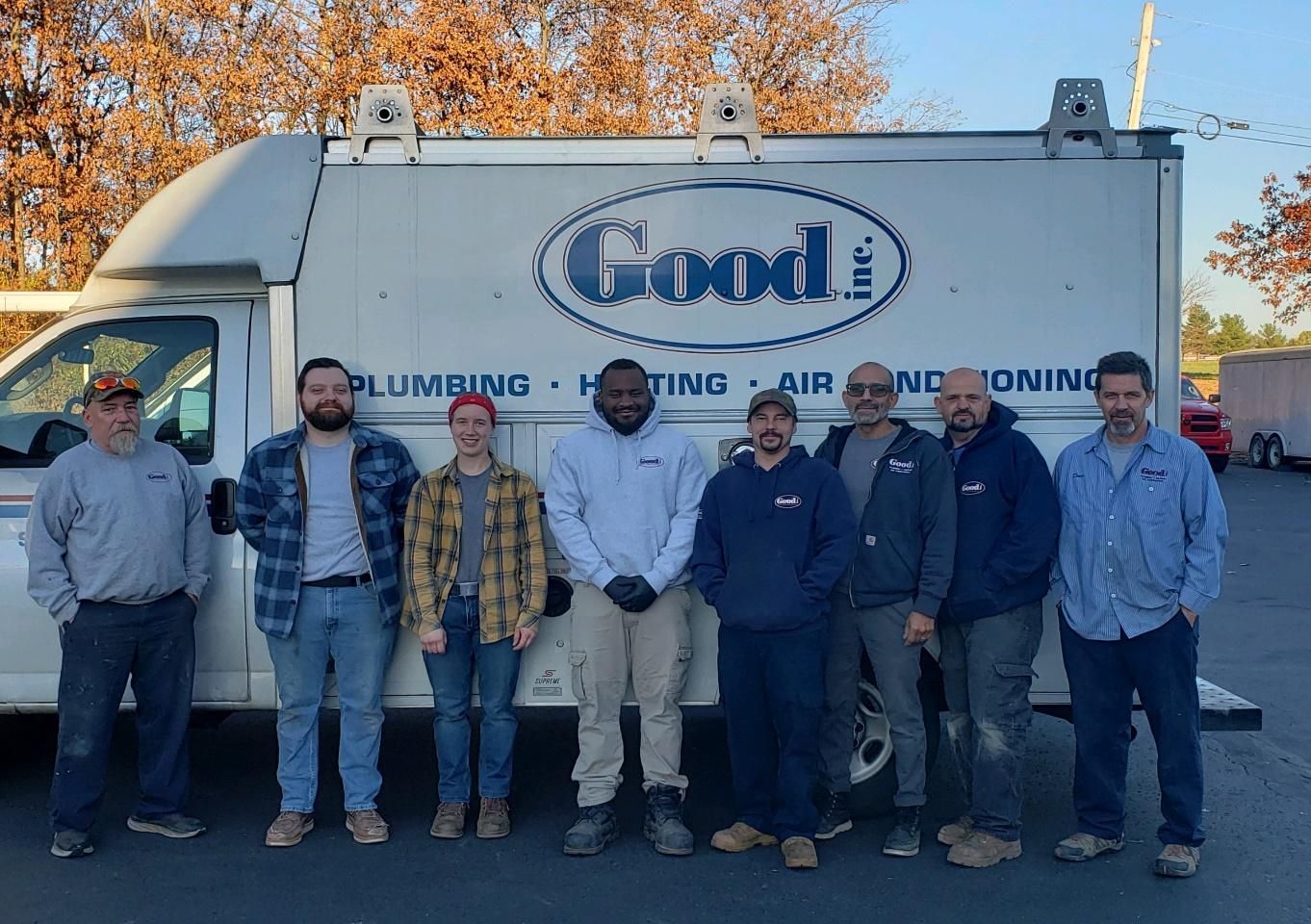 Group of eight people posing in front of a white work truck with 